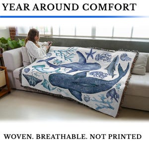 May include: A woven blanket with a marine life design, featuring whales, sharks, and other sea creatures in shades of blue and teal. The blanket is draped over a couch. Text on the image reads: YEAR AROUND COMFORT, WOVEN. BREATHABLE. NOT PRINTED.