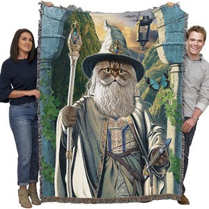 May include: Woven tapestry blanket featuring a cat dressed as a wizard, complete with a staff and sword. The cat has a long white beard and is wearing a wizard hat and robe. The background depicts a fantasy landscape with a lantern and a blue butterfly.