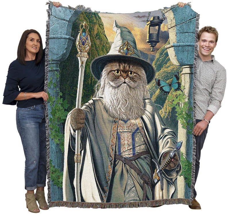 May include: Woven tapestry blanket featuring a cat dressed as a wizard, complete with a staff and sword. The cat has a long white beard and is wearing a wizard hat and robe. The background depicts a fantasy landscape with a lantern and a blue butterfly.