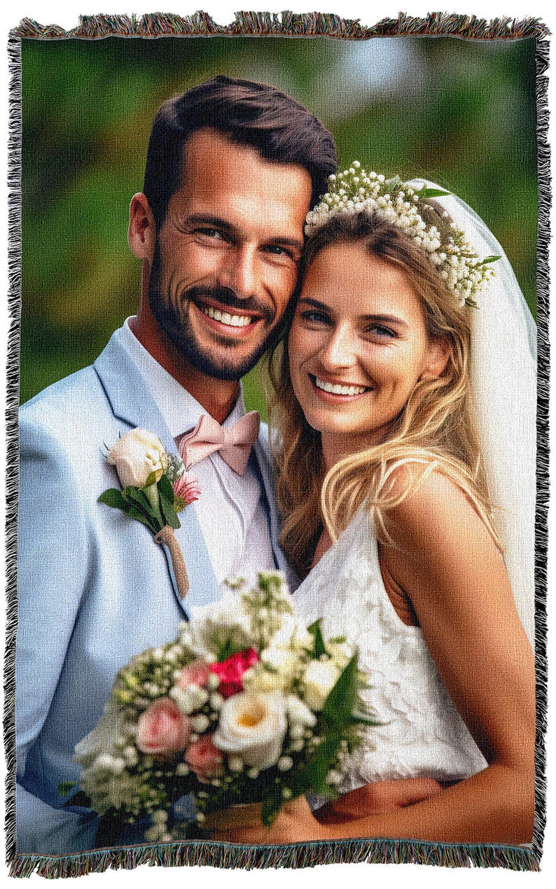May include: A woven throw blanket featuring a smiling couple on their wedding day. The man wears a light blue suit with a pink bow tie and a rose boutonniere. The woman wears a white dress and a floral crown, holding a bouquet.