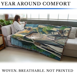 May include: A woven throw blanket with a detailed landscape design featuring a wizard, butterflies, and a river. The blanket is draped over a sofa. Text at the top reads "YEAR AROUND COMFORT" and at the bottom "WOVEN. BREATHABLE. NOT PRINTED."
