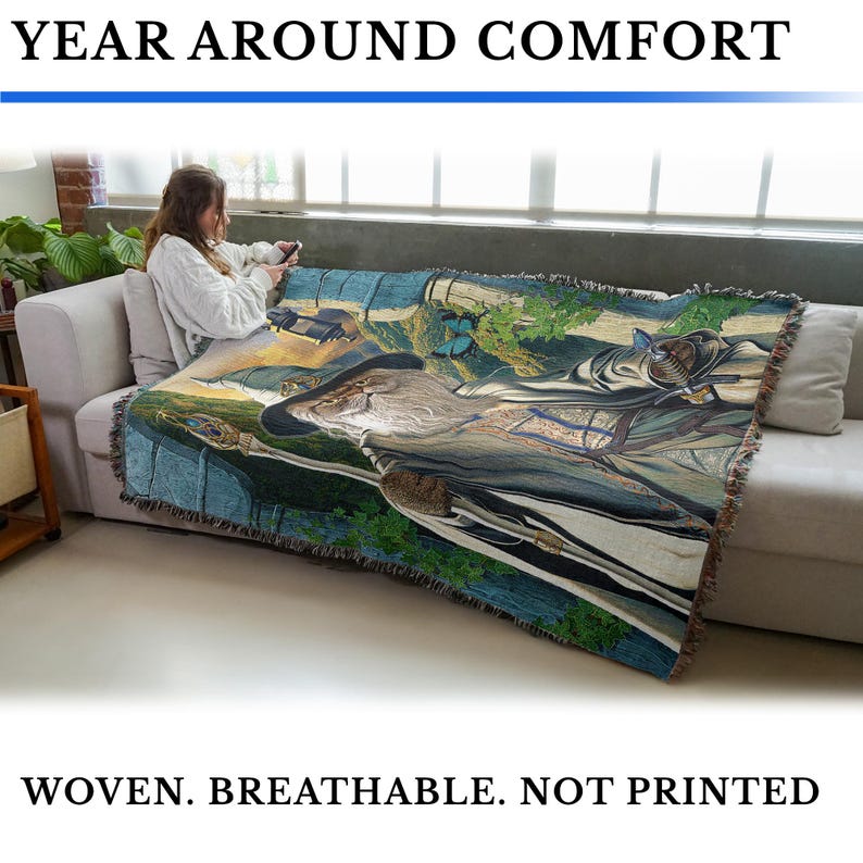 May include: A woven throw blanket with a detailed landscape design featuring a wizard, butterflies, and a river. The blanket is draped over a sofa. Text at the top reads "YEAR AROUND COMFORT" and at the bottom "WOVEN. BREATHABLE. NOT PRINTED."