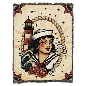 May include: Woven throw blanket with a vintage tattoo design. The artwork depicts a sailor woman, lighthouse, waves, and roses, framed by a rope. The background is beige with nautical star accents and a fringed edge.