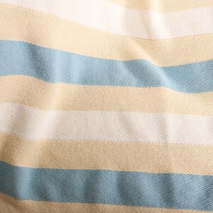 May include: Close-up of a fabric with horizontal stripes in light blue, white, and tan. The fabric has a textured appearance, with the stripes running across the frame. The material appears to be soft and slightly wrinkled.