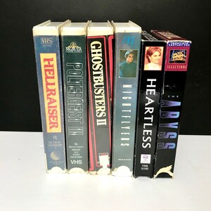 Peut inclure: Une rangée de six cassettes VHS, dont "Hellraiser", "Poltergeist III", "Ghostbusters II", "Nightflyers", "Heartless" et "The Abyss".