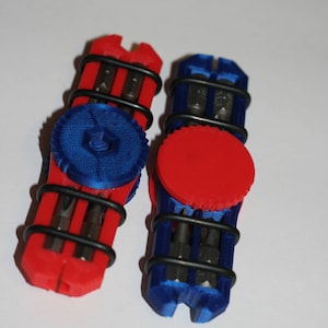 Op de afbeelding: Twee 3D-geprinte gereedschapshouders, één rood en één blauw, elk met een zwarte draadwikkeling. De rode houder heeft een blauwe cirkelvormige bovenkant en de blauwe houder heeft een rode cirkelvormige bovenkant. Beide bevatten meerdere metalen bits.
