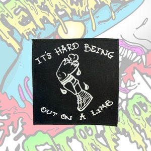 May include: Black and white embroidered patch with the text "It's hard being out on a limb" and a cartoon image of a broken leg in a cast and a shoe.