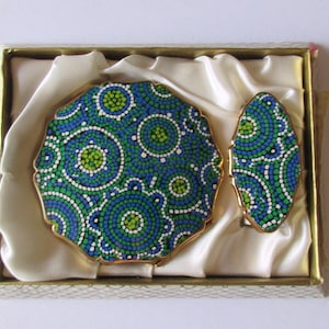 Peut inclure: Un miroir de poche et un petit compact assorti dans un coffret doublé de satin blanc. Les deux sont décorés d'un motif en mosaïque bleu, vert et blanc.
