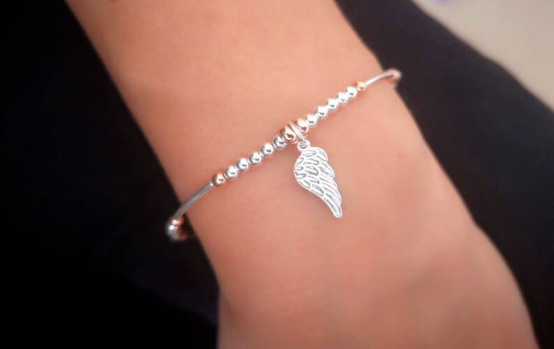 Puede incluir: Una pulsera de plata con un dije de ala de &aacute;ngel de plata. La pulsera est&aacute; hecha de peque&ntilde;as cuentas de plata y oro rosa.