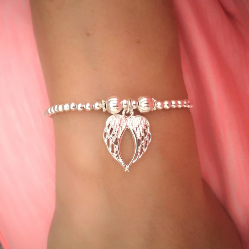 A silver beaded bracelet or anklet with a silver angel wing charm.