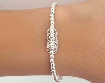 May include: A silver beaded bracelet featuring a central cluster of five interlocking silver rings. The bracelet is constructed from a continuous strand of small, polished, spherical silver beads that are strung together in a single line.
