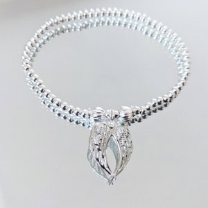 A silver beaded bracelet or anklet with a silver angel wing charm.