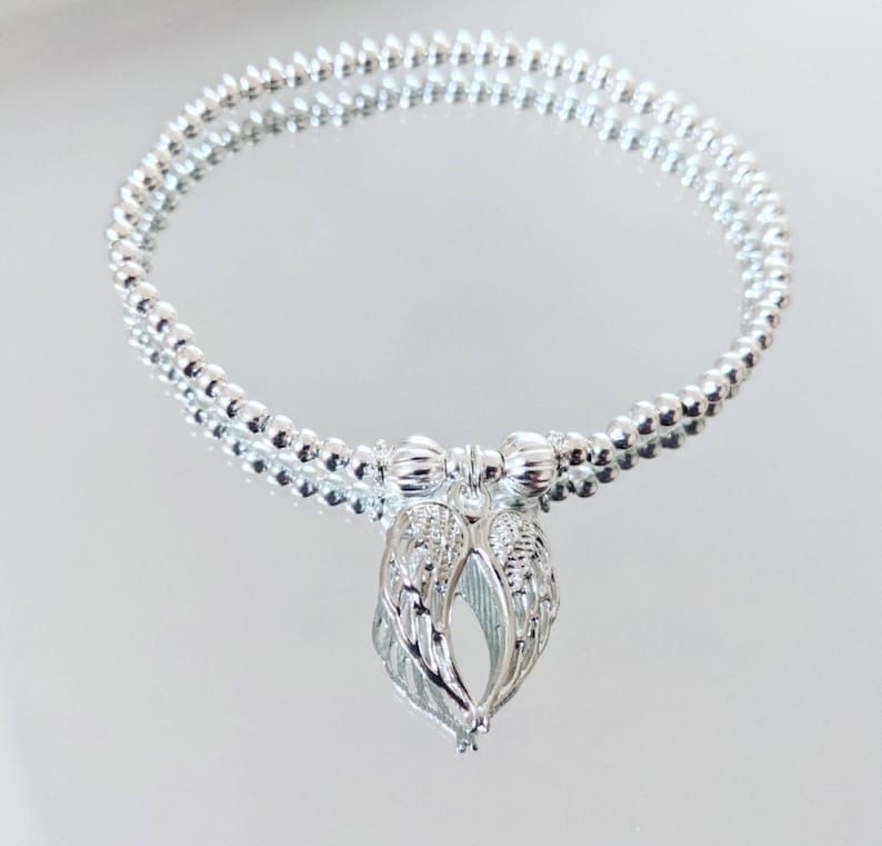 A silver beaded bracelet or anklet with a silver angel wing charm.