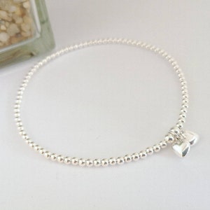 Könnte beinhalten: Ein silbernes Perlenarmband mit zwei kleinen silbernen Herzanhängern.