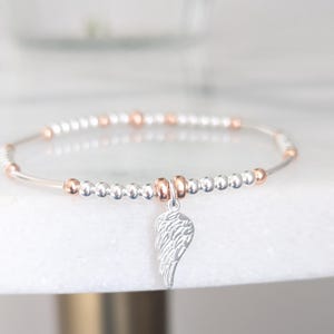Puede incluir: Un brazalete de cuentas de plata y oro rosa con un dije de ala de &aacute;ngel de plata.