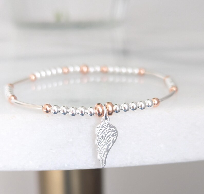 Puede incluir: Un brazalete de cuentas de plata y oro rosa con un dije de ala de &aacute;ngel de plata.