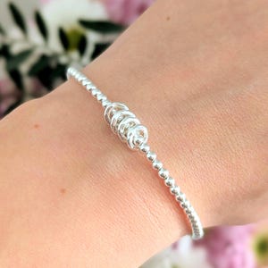 May include: A silver bracelet featuring small, round beads and a central spiral design. The bracelet's design is delicate and elegant. The spiral detail adds a unique touch to the jewelry. The bracelet is suitable for everyday wear.