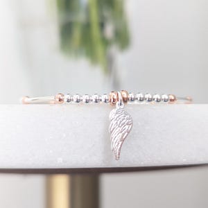 Puede incluir: Un brazalete de cuentas de plata y oro rosa con un dije de ala de &aacute;ngel de plata.