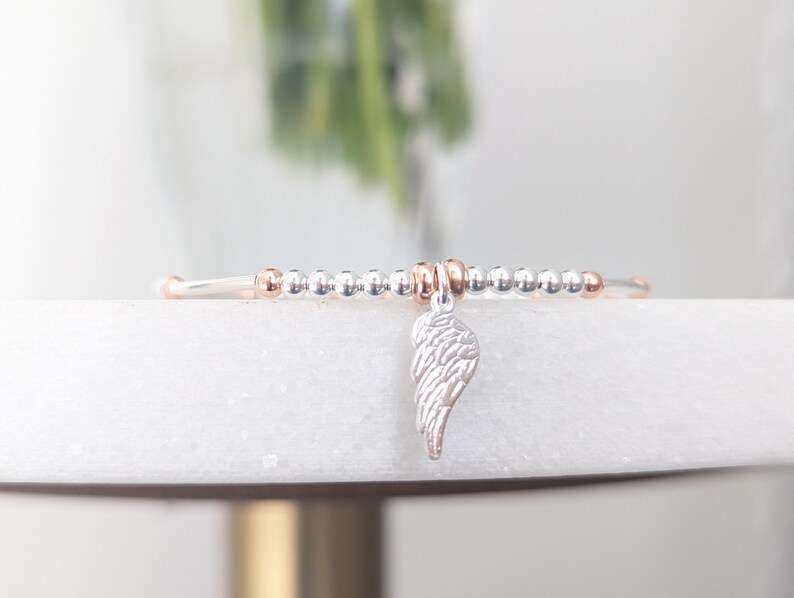 Puede incluir: Un brazalete de cuentas de plata y oro rosa con un dije de ala de &aacute;ngel de plata.