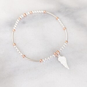 Puede incluir: Una pulsera de plata con un dije de ala de &aacute;ngel de plata. La pulsera est&aacute; hecha de peque&ntilde;as cuentas de plata y oro rosa.