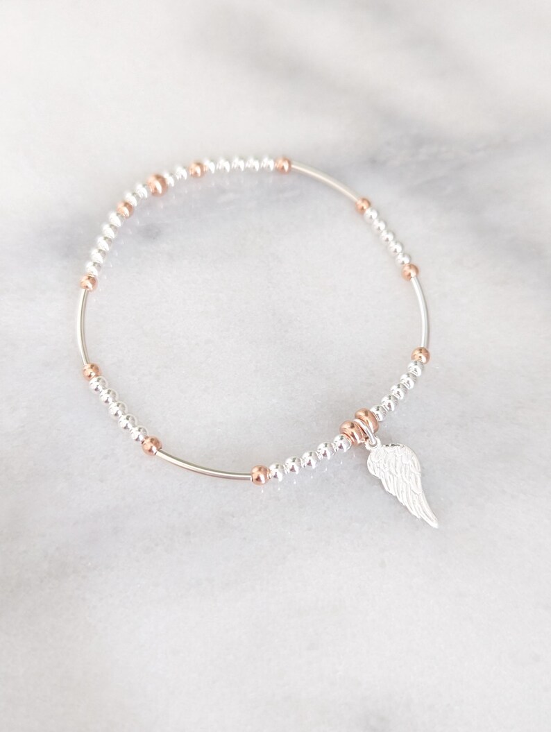 Puede incluir: Una pulsera de plata con un dije de ala de &aacute;ngel de plata. La pulsera est&aacute; hecha de peque&ntilde;as cuentas de plata y oro rosa.