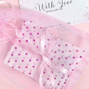 A pink polka dot gift bag with a white satin ribbon. The bag is tied with a bow and has a white card with the text 'With Love Jewellery UK' on it.