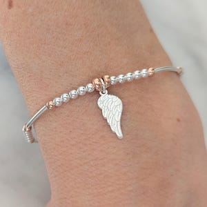 Puede incluir: Un brazalete de cuentas de plata y oro rosa con un dije de ala de &aacute;ngel de plata.