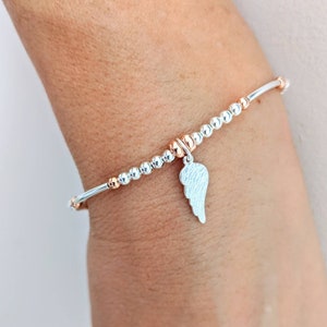 Puede incluir: Una pulsera de cuentas de plata y oro rosa con un dije de ala de &aacute;ngel de plata. La pulsera est&aacute; en la mu&ntilde;eca.