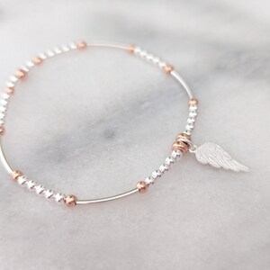 Puede incluir: Un brazalete de plata con peque&ntilde;as cuentas de plata y oro rosa y un dije de ala de &aacute;ngel de plata.