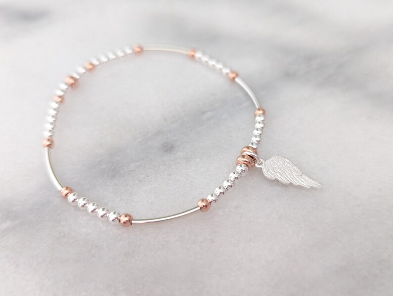 Puede incluir: Un brazalete de plata con peque&ntilde;as cuentas de plata y oro rosa y un dije de ala de &aacute;ngel de plata.