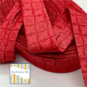 May include: A roll of red bias binding with a repeating floral pattern. The fabric is folded over, ready for sewing projects. The bias tape is in a close-up shot, showing the detail of the design. The text "BiasBinding-UK" is visible in the lower left corner.