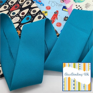 May include: A wide strip of solid teal bias binding fabric folded in a serpentine shape, positioned over two patterned fabric swatches featuring black and white teapots and colourful cars. A square logo with the text BiasBinding-UK is visible.