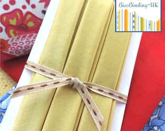 May include: Three rolls of yellow bias binding tape tied together with a brown ribbon. The ribbon has a brown dashed line down the center. The tape is on a white background.