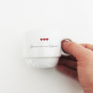May include: White ceramic coffee mug with a black inscription that reads "Jamais sans mes Copines" and three red hearts.