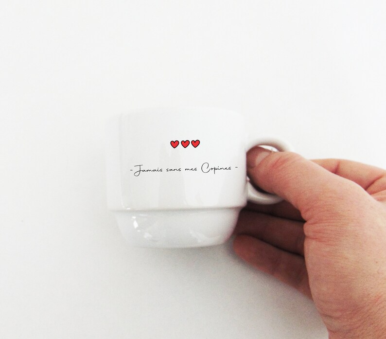 May include: White ceramic coffee mug with a black inscription that reads "Jamais sans mes Copines" and three red hearts.