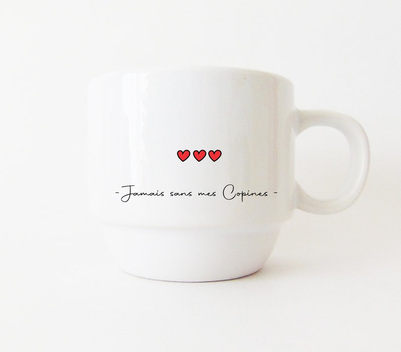 May include: White ceramic mug with a black inscription that reads "Jamais sans mes Copines" and three red hearts.