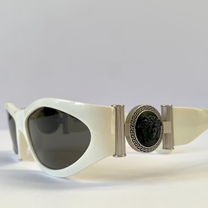 May include: White sunglasses with a black and silver Medusa head emblem on the side.