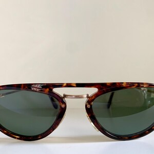 Puede incluir: Gafas de sol aviador de carey con lentes verdes y la marca Ray-Ban en la lente izquierda.