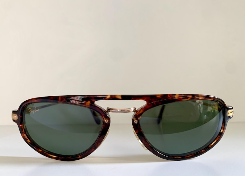 Puede incluir: Gafas de sol aviador de carey con lentes verdes y la marca Ray-Ban en la lente izquierda.