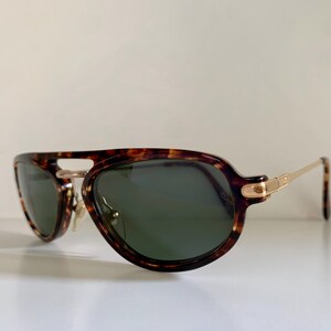 Puede incluir: Gafas de sol aviador de carey con detalles dorados y lentes verdes.
