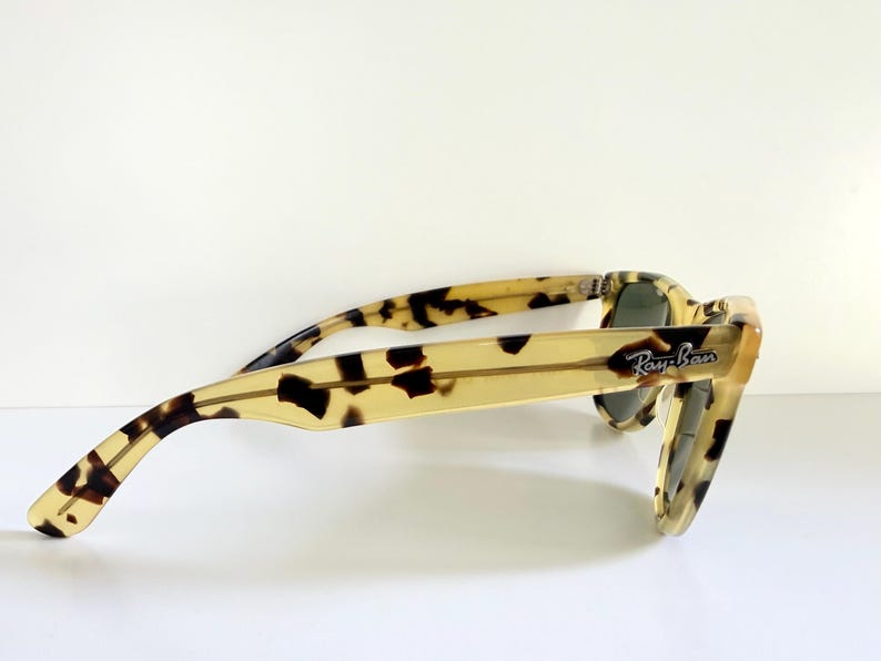 May include: A pair of Ray-Ban sunglasses with a light brown and black tortoiseshell pattern. The sunglasses have a classic square frame and dark lenses. The Ray-Ban logo is visible on the temple.