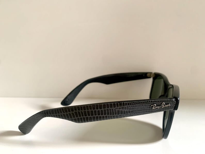 May include: Black sunglasses with a textured, dark gray pattern on the arms. The Ray-Ban logo is visible on the side. The lenses are dark, and the frames are black.
