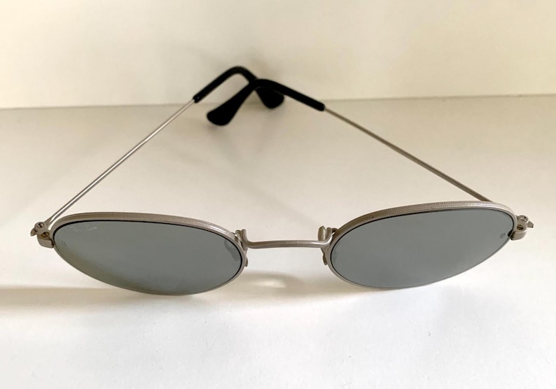 Puede incluir: Gafas de sol ovaladas plateadas con lentes espejados.