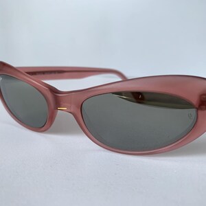 Peut inclure: Lunettes de soleil roses en forme d'&oelig;il de chat avec des verres gris fonc&eacute;. Les montures ont un aspect translucide. Les lunettes de soleil ont un design r&eacute;tro classique. Les verres sont l&eacute;g&egrave;rement incurv&eacute;s.