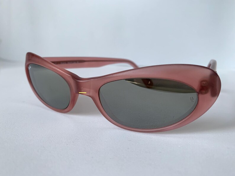 Peut inclure: Lunettes de soleil roses en forme d'&oelig;il de chat avec des verres gris fonc&eacute;. Les montures ont un aspect translucide. Les lunettes de soleil ont un design r&eacute;tro classique. Les verres sont l&eacute;g&egrave;rement incurv&eacute;s.