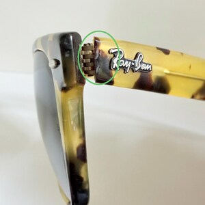 May include: Close-up of Ray-Ban sunglasses with a tortoise shell pattern. The frame is a mix of brown and yellow, with the Ray-Ban logo visible on the temple. The hinge is a silver color.