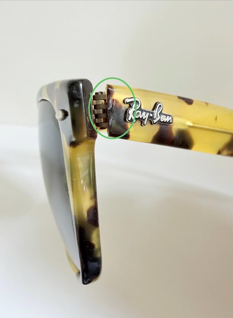May include: Close-up of Ray-Ban sunglasses with a tortoise shell pattern. The frame is a mix of brown and yellow, with the Ray-Ban logo visible on the temple. The hinge is a silver color.