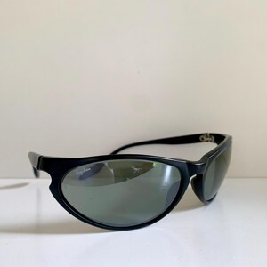 May include: Black sunglasses featuring a wrap-around frame design with dark tinted lenses. The Ray-Ban logo is printed in white on the upper corner of the right lens. The frame has a smooth, matte finish with curved temples and integrated nose pads.