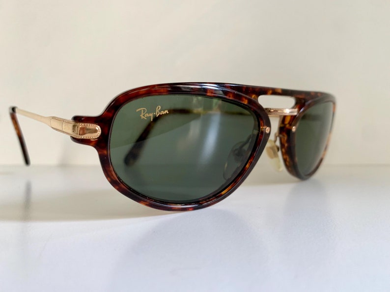 Puede incluir: Gafas de sol Ray-Ban de carey con detalles dorados y lentes verdes.