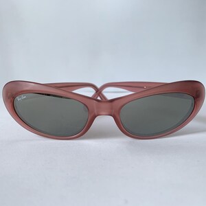 Peut inclure: Lunettes de soleil mauves en forme d'&oelig;il de chat. Les lunettes ont des verres gris fonc&eacute; et le logo Ray-Ban sur la lentille gauche. La monture est de couleur unie et translucide. Sur fond blanc.